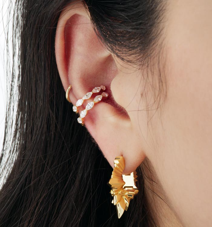 Gros plan sur une oreille avec une composition de boucles d'oreilles Maria Tash, des studs, des anneaux, des pendents agencés tout autour de l'oreille