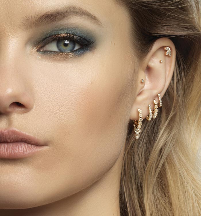 Model wearing studs and rings of all sizes on every part of the ear, whether the helix at the top, the tragus just below or even the conch further inside.